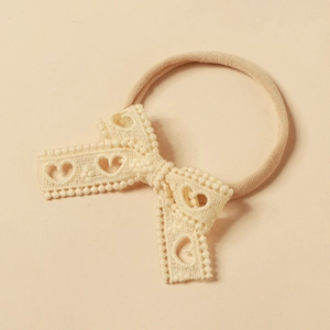 Dettaglio del fiocco in pizzo beige con motivi a cuore su una fascia elastica per neonati