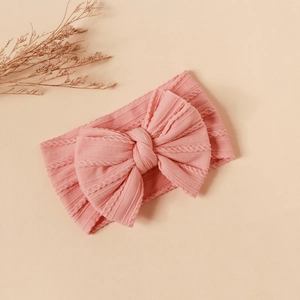 Detail of pink knitted baby headband featuring cable texture and large double bow