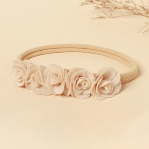 Détail du bandeau en nylon pour bébé avec cinq roses en tissu beige alignées avec soin