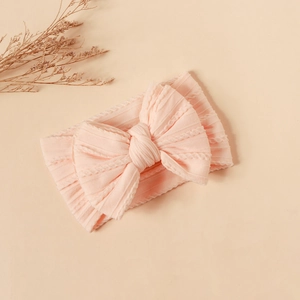 Detailed close-up of soft peach rib-knit baby headband with a large bow on warm background