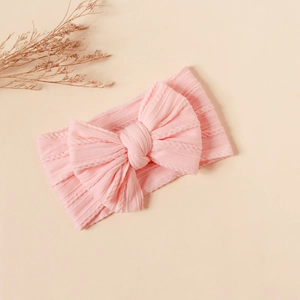 Macro detail of pink knitted nylon baby headband showing soft cable knit texture and bow