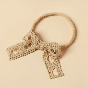 Dettaglio macro di una fascia in pizzo beige con ricami a forma di cuore e fiocco