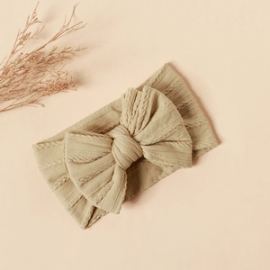 Detailed cable knit texture and large bow on a soft nylon baby headband in beige color