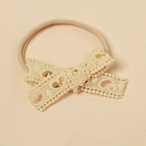 Detail of baby headband featuring lace bow with hollow heart pattern and nylon band