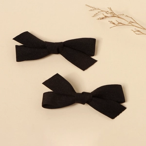 Macro detail of two solid black fabric bow hair clips on a minimalist beige background