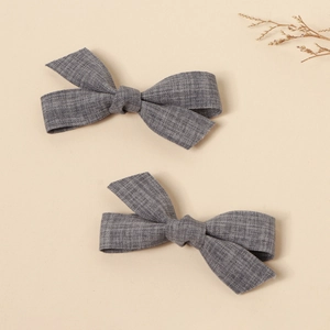 Detail of two grey handmade linen bow hair clips on a minimalist beige background