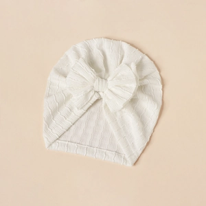Detailed view of white newborn turban hat with bow and soft textured elastic fabric