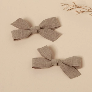 Detailed macro view of handmade linen bow hair clips in earthy khaki colors on beige background