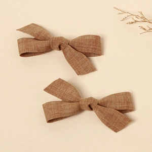 Detail of two handmade brown linen bow hair clips with natural fabric texture