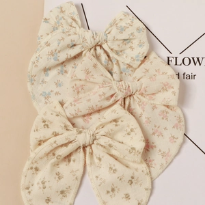 Dettaglio di tre fermagli per capelli con fiocco floreale nei colori rosa blu e verde