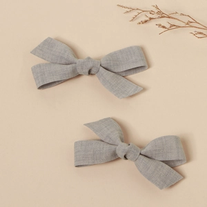 Detail of two handmade grey linen fabric bow hair clips on a minimalist beige background