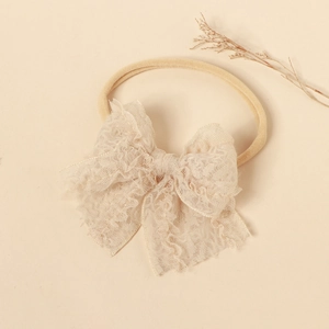 Close-up of soft lace bow baby headband with elastic nylon band on beige background
