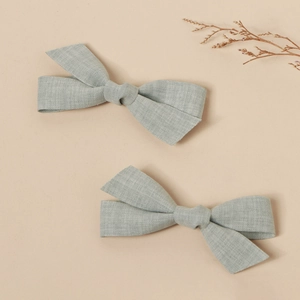 Detail of light blue-grey linen bow hair clips showing natural fabric texture on beige background