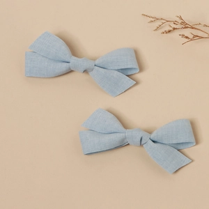 Detail of two light blue linen bow hair clips with textured fabric on a natural background