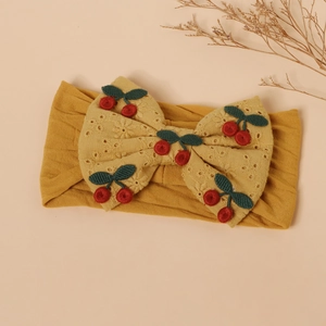 Close-up of yellow baby headband with hollow-out bow and embroidered cherry detail