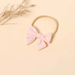Detailed close-up of a pink bow baby headband with intricate white floral embroidery on nylon