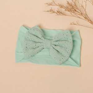 Detail view of mint green baby headband featuring eyelet embroidery and a large bow