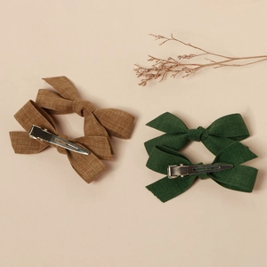 Handmade brown and dark green fabric bow hair clips with metal duckbill clips on beige background