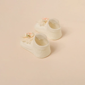 Détail des chaussons-chaussettes crème pour bébé avec fleur rose 3D et ruban vert soyeux