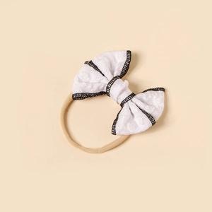 Close-up of white lace bow headband with black trim and soft nylon elastic band for baby