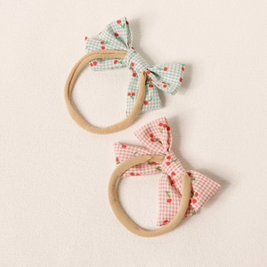Détail de deux bandeaux pour bébés avec nœuds à carreaux cerise et bandes en nylon