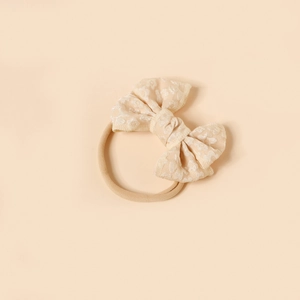 Detail of soft beige nylon baby headband featuring a jacquard floral bow texture