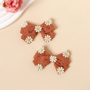 Détail macro de barrettes à nœuds en coton marron avec broderie de marguerites blanches