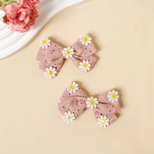 Détail de barrettes à nœuds en coton rose avec broderies de marguerites sur tissu doux