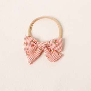 Gros plan du bandeau bébé en nylon avec nœud à carreaux orange et motifs de cerises