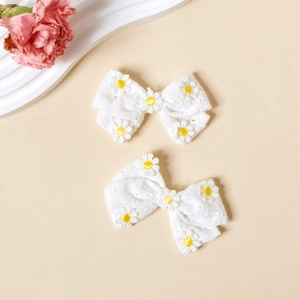 Détail de deux barrettes noeuds en coton blanc avec motifs marguerites brodés