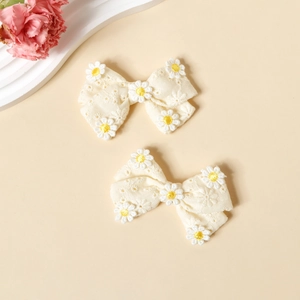 Gros plan de pinces à cheveux à nœud en coton blanc crème avec broderie marguerite