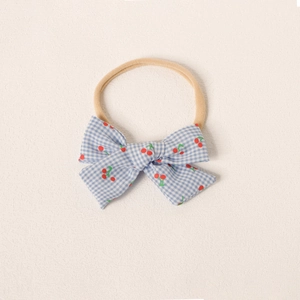Détail d'un bandeau pour bébé en nylon souple avec nœud à carreaux et motif cerise