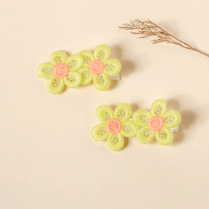 Detail view of two yellow embroidered floral hair clips with a warm beige background