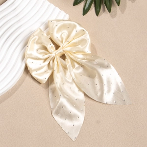Détail du nœud papillon en satin crème avec strass et longs rubans sur fond texturé