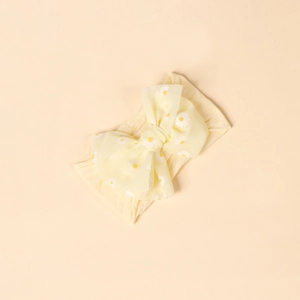 Detail of yellow baby bow headband featuring fresh white daisy print on soft fabric