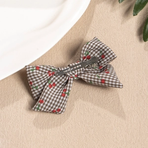 Plaid fabric bow hair clip with red cherry pattern on a warm beige background