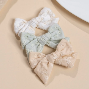 Detail of three handmade cotton bow hair clips with delicate floral embroidery patterns