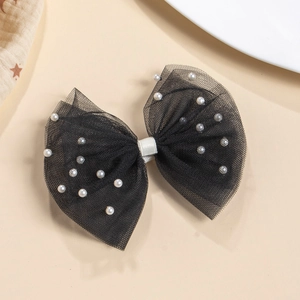 Détail d'un nœud à cheveux en tulle noir orné de perles blanches sur fond beige