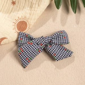 Close-up of black and white checkered fabric bow hair clip with red cherry embroidery