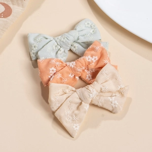 Detail of three handmade cotton bow hair clips with white floral embroidery in soft colors
