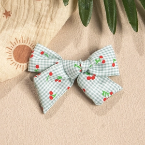 Detailed view of a green plaid fabric bow hair clip with bright red cherry pattern