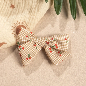 Detailed view of yellow plaid fabric bow hair clip with cherry prints on fabric