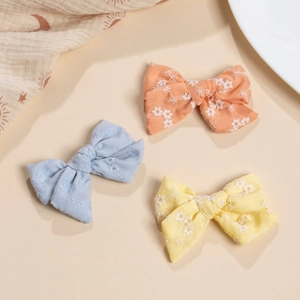 Three handmade cotton bow hair clips with white floral embroidery in orange, blue and yellow