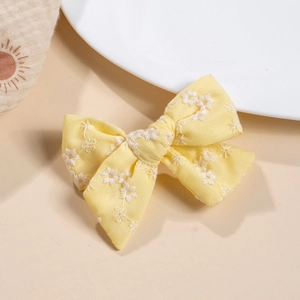 Detail of yellow cotton bow hair clip with delicate white floral embroidery on beige fabric