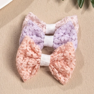 Detailed macro view of three lace embroidered bow hair clips in soft pastel colors