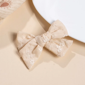 Close-up of beige cotton bow hair clip featuring delicate white floral embroidery detail