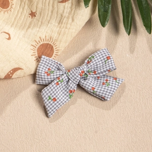 Detail of grey plaid bow hair clip with red cherry patterns on a beige textured background