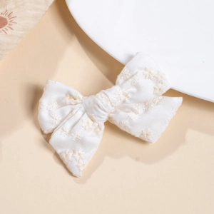 Detail of white cotton bow hair clip with delicate light brown floral embroidery patterns