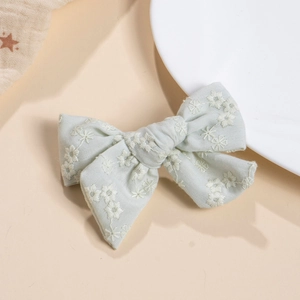 Detailed close-up of handmade mint green fabric bow hair clip with white floral embroidery