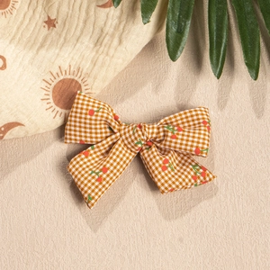 Detail of gingham bow hair accessory with cherry print on beige sand background